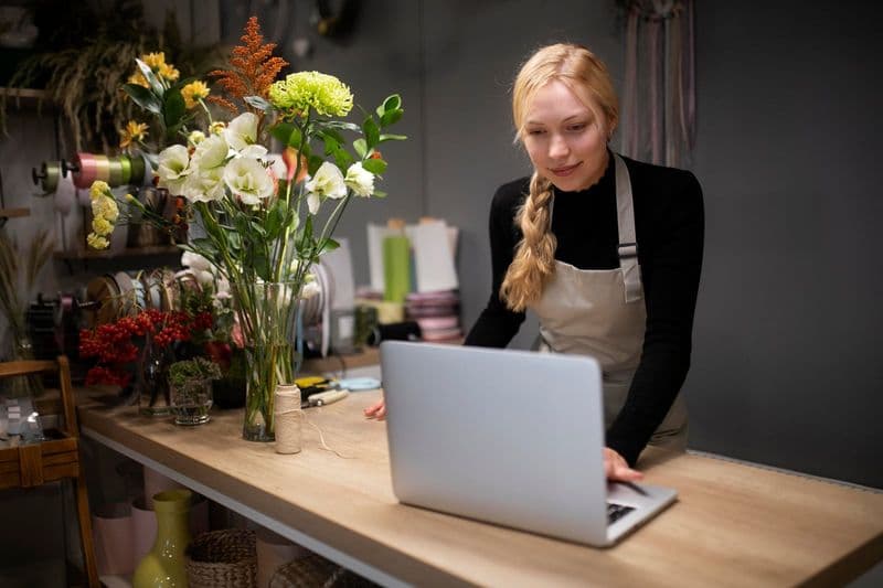 Dona de pequeno negócio usando notebook no balcão da sua loja de flores