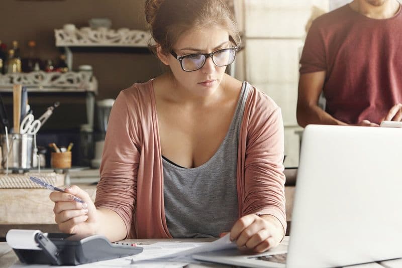 Empreendedora adulta organizando as contas do negócio com notebook e calculadora sobre a mesa