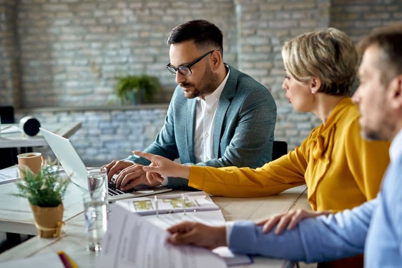 Consultor analisa documentos e cálculo de impostos com clientes em reunião no escritório